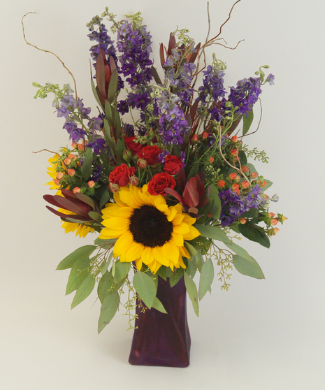 Sunflowers, purple spray roses, hypericum berries and curly willow in a colored vase.