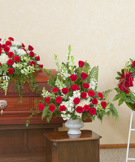 Three funeral flower arrangements: a red and white casket spray, urn and wreath. 