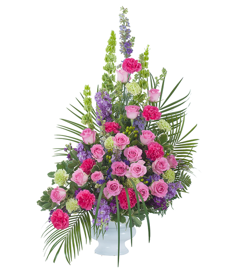 Sympathy crescent spray of pink and purple flowers in a white urn. 