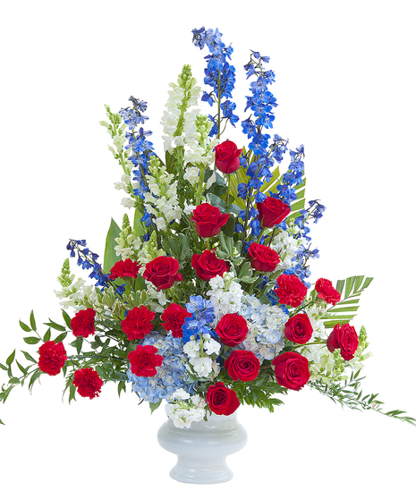 Patriotic sympathy display of red, white and blue flowers in a white urn. 