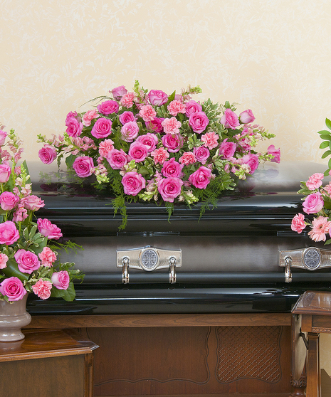 Trio of funeral arrangements: One casket spray and two urn arrangements of pink flowers.