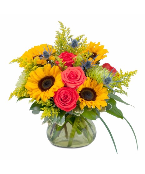 Sunflowers, roses and accent flowers in a clear glass vase.