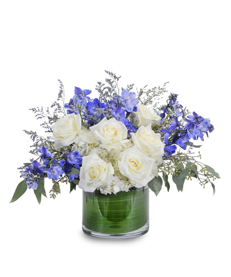 White roses, hydrangea and blue delphinium in a leaf-lined cylinder vase.