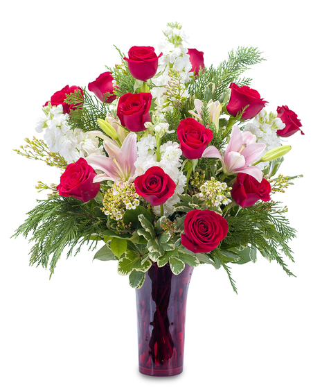 Ruby red vase of lilies and red roses accented with winter greenery